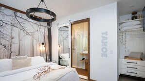 A modern bedroom with a large bed, a chandelier, a wardrobe, and a bathroom visible through an open door. - Lake View Home with Private Hot Tub (Tahoma)