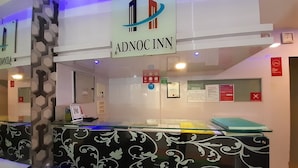 Un mostrador de recepción con una encimera estampada en blanco y negro, un cartel que dice "ADNOC INN" y varios carteles informativos en la pared.