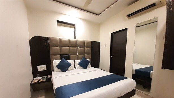 Una habitación de hotel con cama, mesita de noche, espejo y puerta.