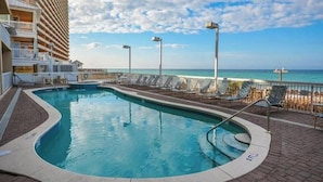 A pool area with a view of the ocean, a building with balconies, and a clear sky.