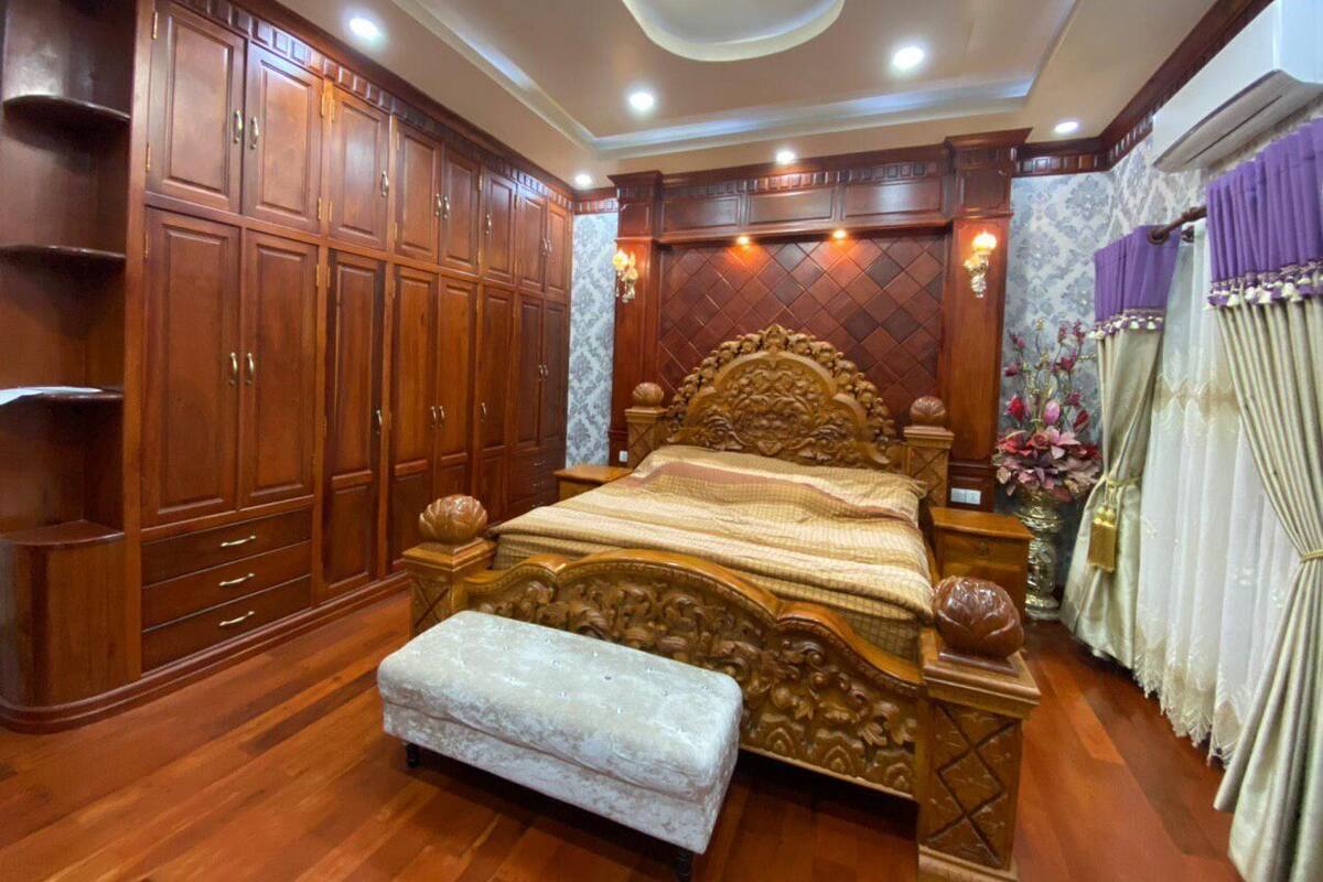 A bedroom with a large wooden wardrobe, a bed with an ornate headboard, and a bench.