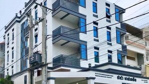 Un edificio de varios pisos con balcones, un letrero en idioma local y un vehículo estacionado.