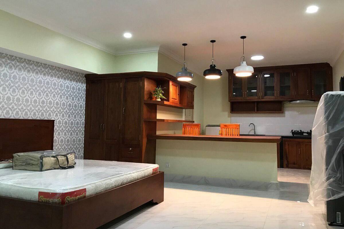 A bedroom with a bed, a small kitchenette, wooden cabinets, and pendant lights.