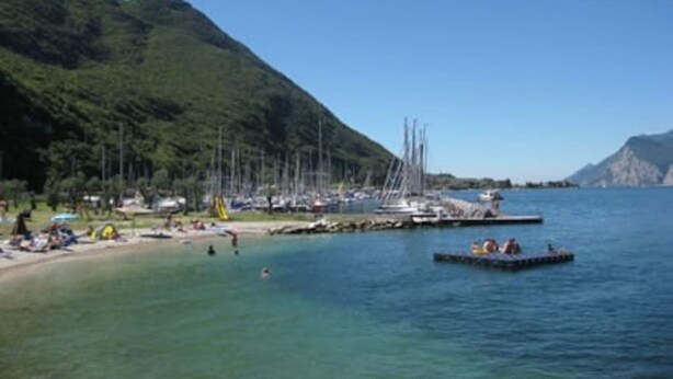Une zone côtière où des bateaux sont amarrés, avec une plage et un paysage montagneux en arrière-plan.