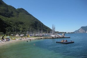 Une zone côtière où des bateaux sont amarrés, avec une plage et un paysage montagneux en arrière-plan.