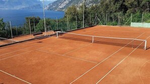 Un court de tennis avec un filet, des bancs et une vue sur la mer et les montagnes.