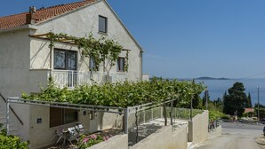 Una casa de dos pisos con un balcón, un ventanal pequeño y vista al mar.