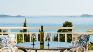 Una mesa redonda con dos copas de vino y una botella en un balcón con vista al agua.