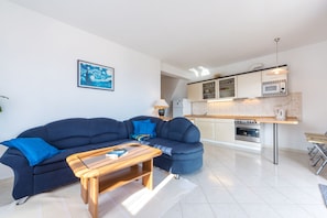 A modern living room with a sofa, coffee table, and a kitchen area with cabinets and appliances.