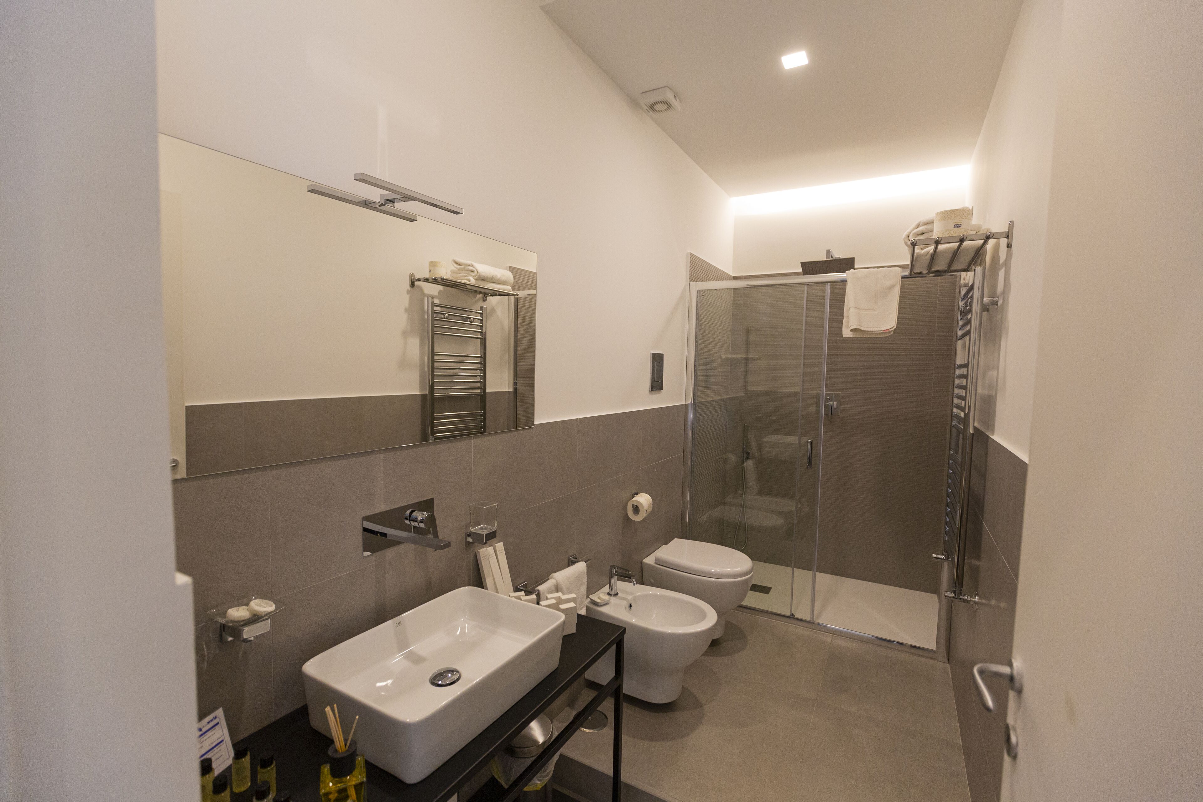 Un baño moderno con un espejo grande, un lavabo, un bidé y una ducha con mampara de vidrio.