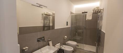 A modern bathroom with a large mirror, a sink, a bidet, and a glass-enclosed shower.