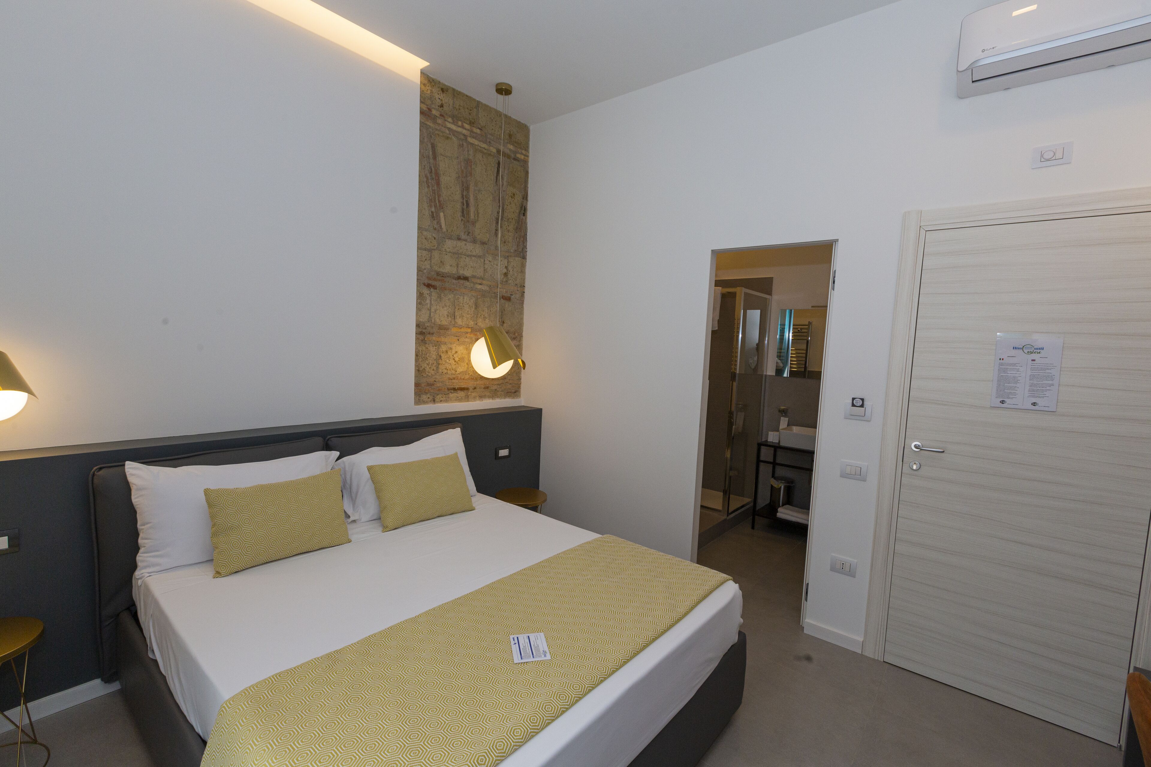 A hotel room with a bed, bedside tables, a wall-mounted light, and a door.