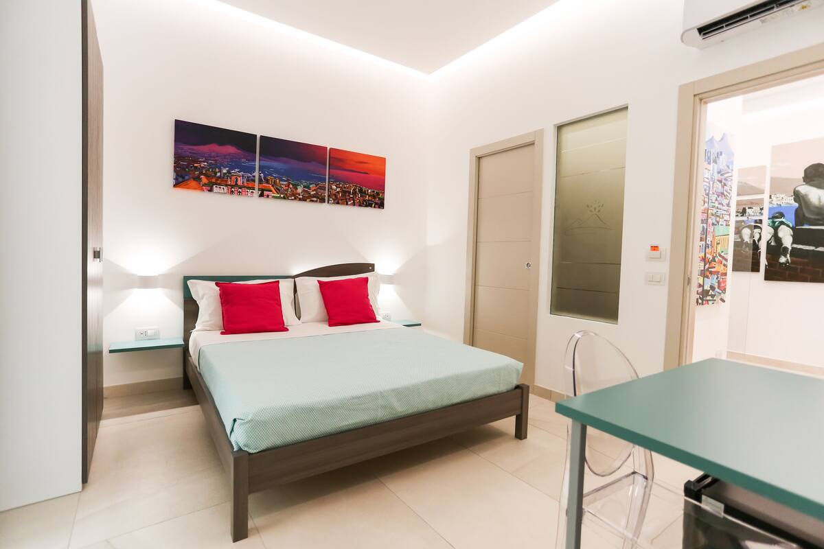 Un dormitorio con una cama, dos lámparas de noche, una mesita de noche, una mesa de vidrio y una puerta con un cartel.