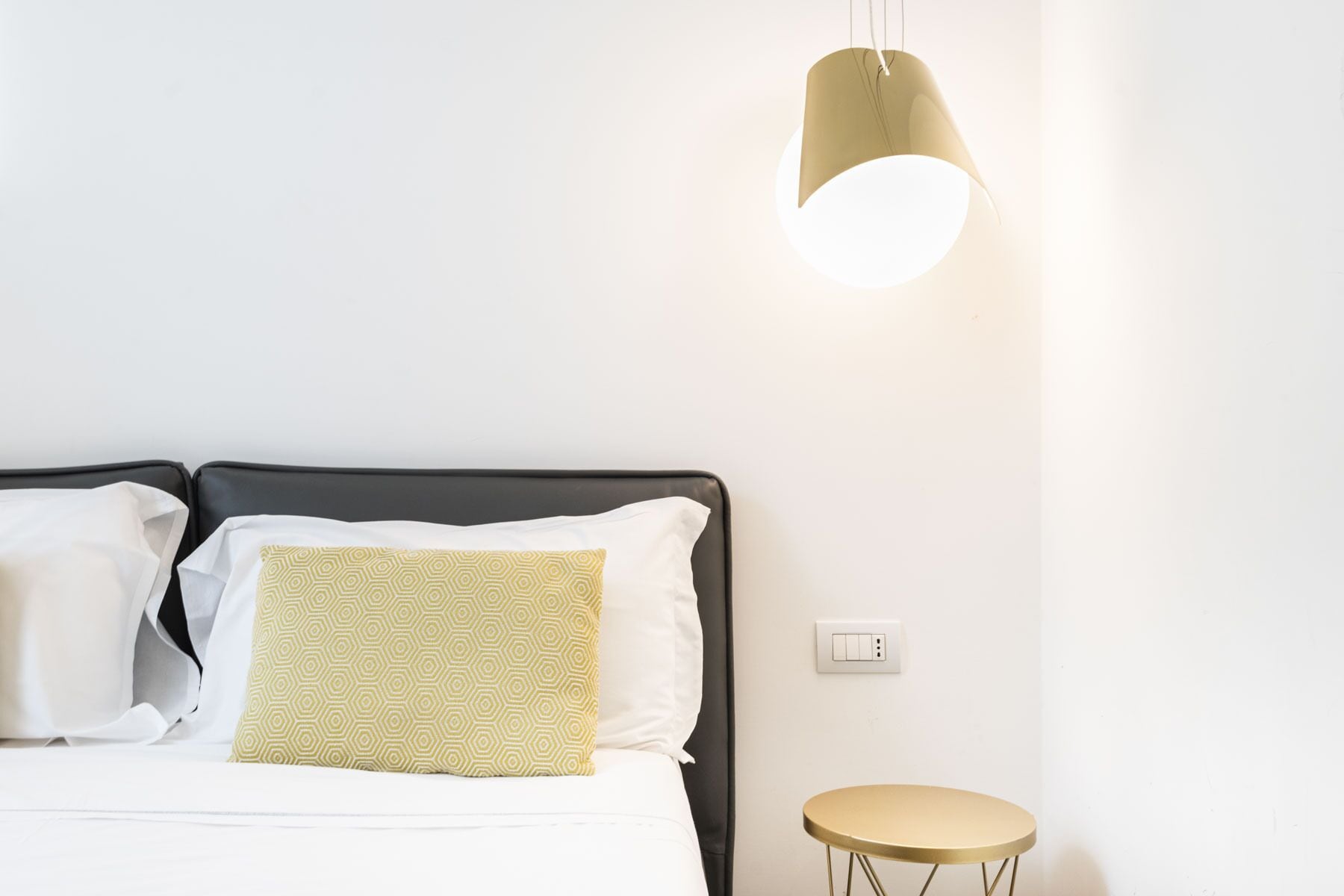 Una cama bien hecha con dos almohadas, una mesita de noche y una lámpara colgante.