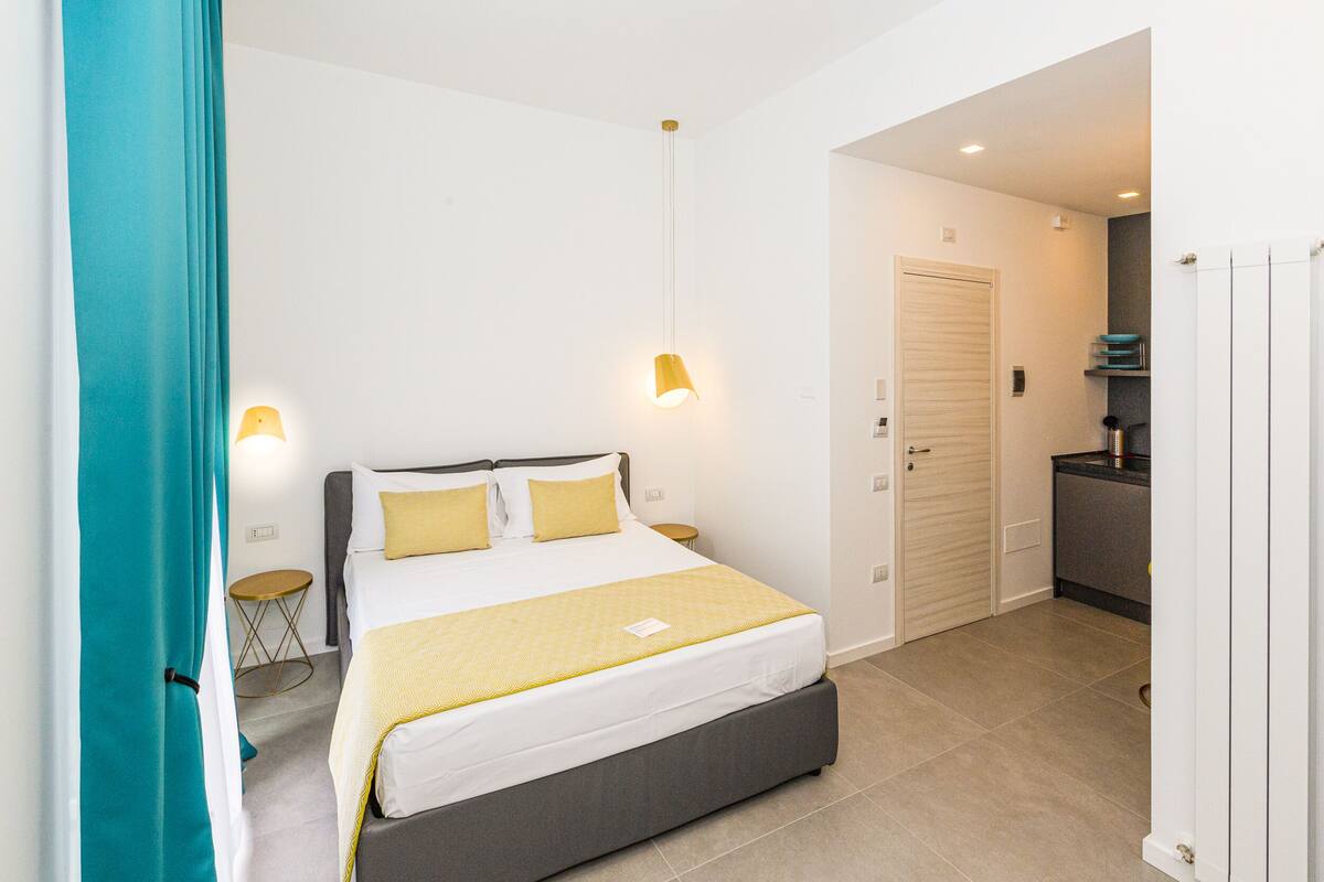 Un dormitorio moderno con cama, lámparas de noche, una mesita redonda y una puerta que da al baño.