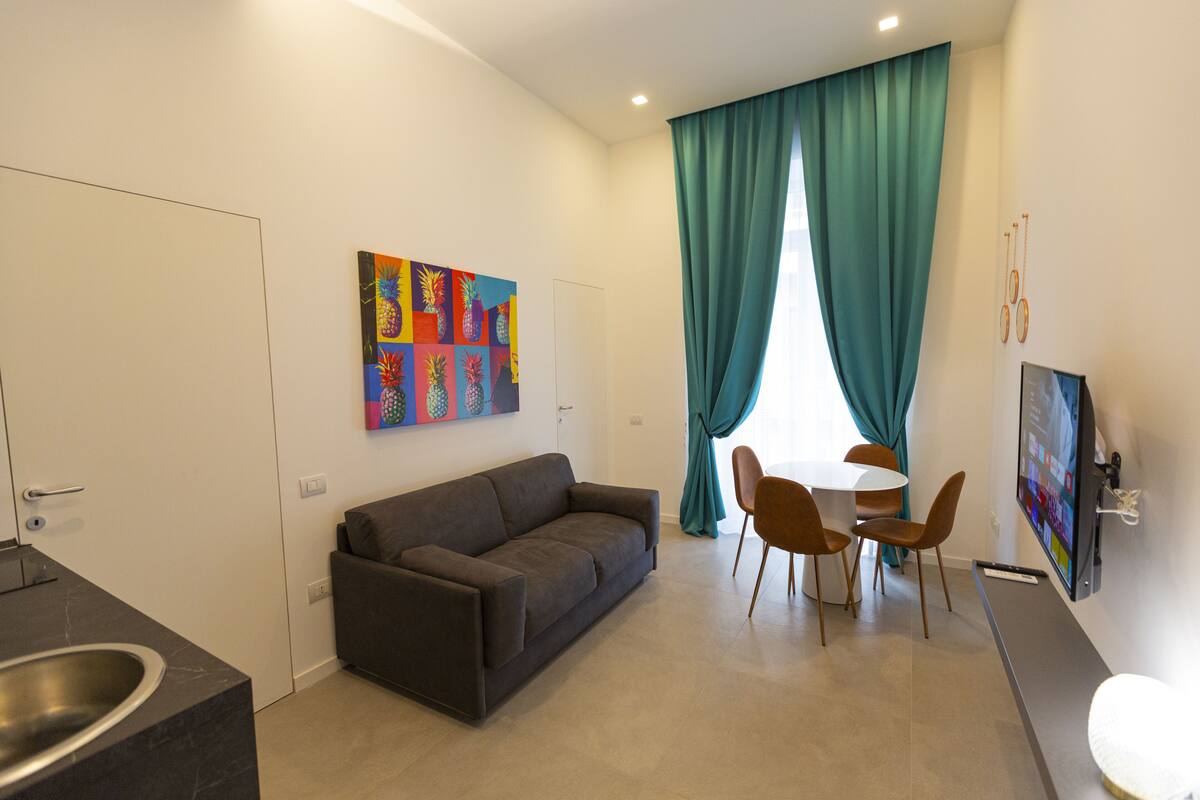 Una sala moderna con sofá, mesa de comedor, sillas, televisor y una obra de arte colorida en la pared.
