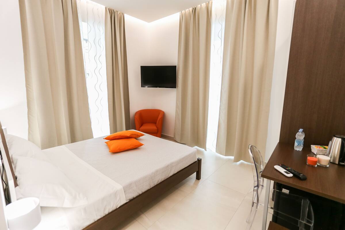 Una habitación de hotel con cama, una silla, escritorio y control remoto, una botella y una taza.