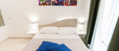 A hotel room with a bed, two pillows, a wall-mounted artwork, and two bedside lamps.