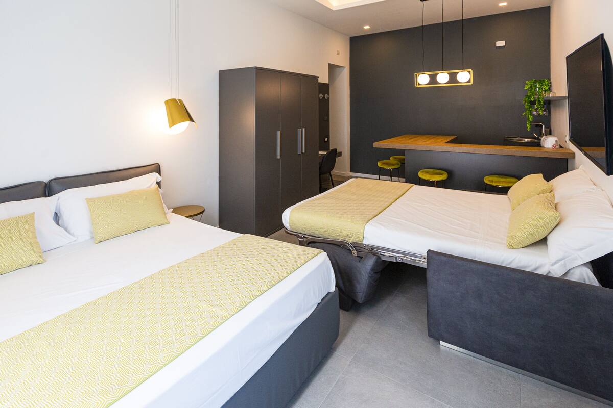 Una habitación de hotel moderna con una cama grande, un escritorio y una pequeña kitchenette.