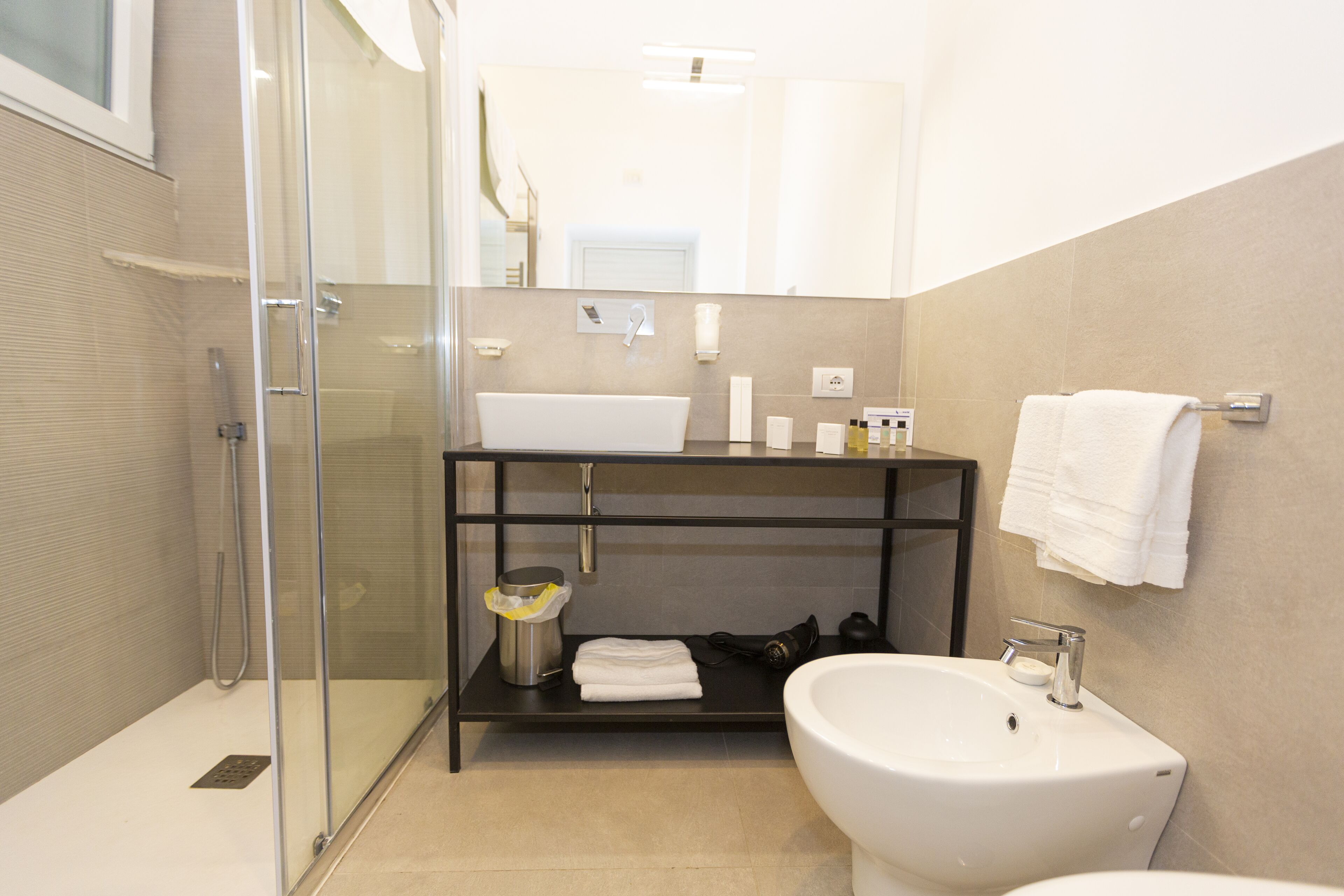 A modern bathroom with a glass-enclosed shower, a white sink, and a black shelf with toiletries.