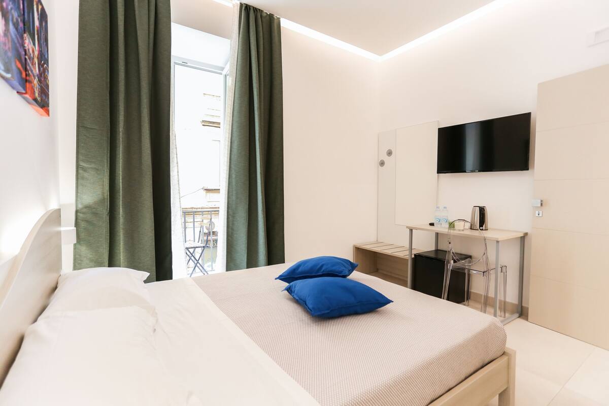 Una habitación de hotel moderna con cama, escritorio y televisor de pantalla plana, y vistas al exterior.