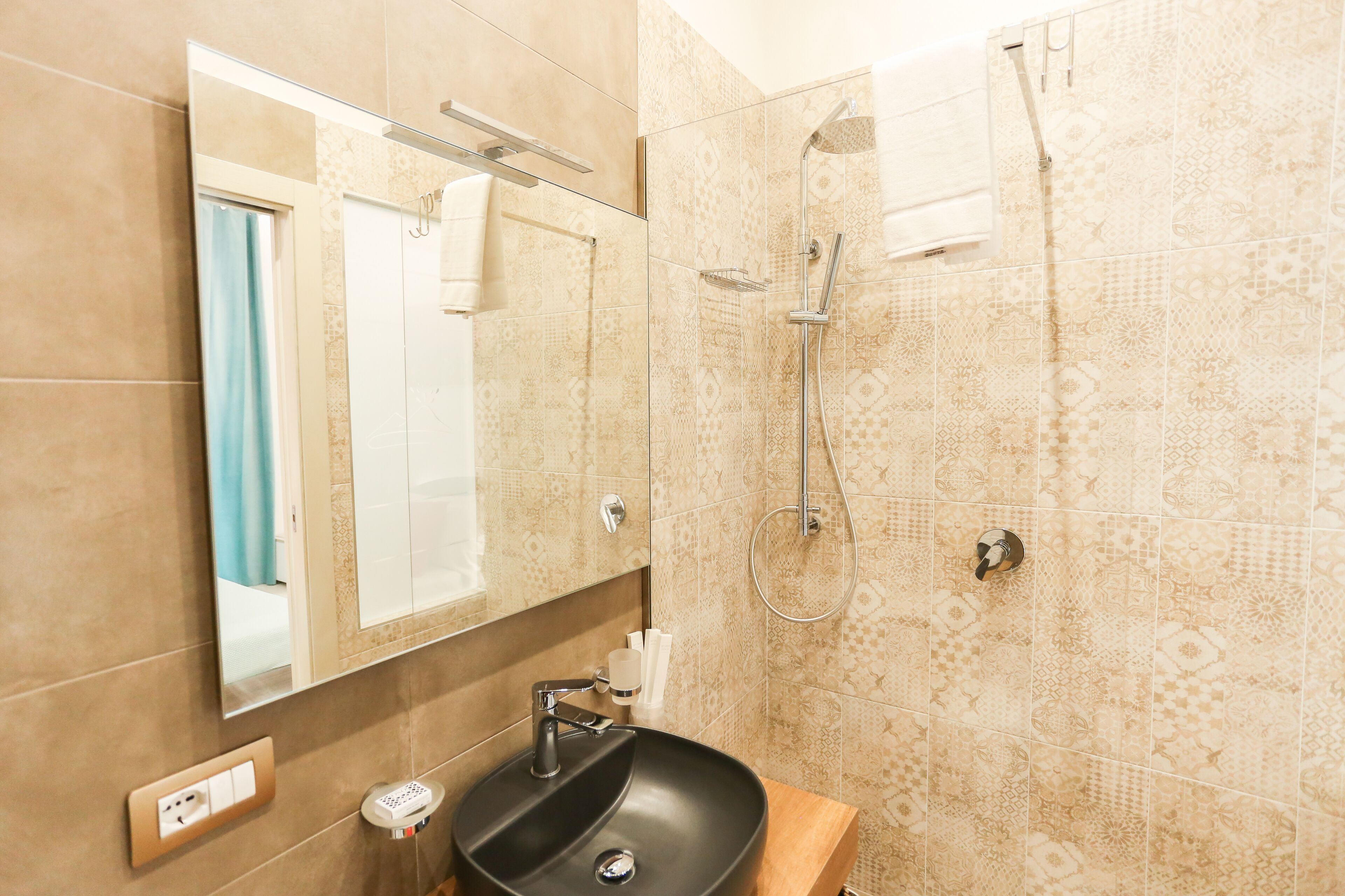 A bathroom with a black sink, a mirror, a shower, and patterned tiles.