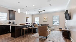A modern kitchen with dark cabinetry, a central island with stools, a ceiling fan, and recessed lighting. - Modern 4BR Mid-City home with heated pool & balcony. Free parking, walk to streetcar & parades. (New Orleans)