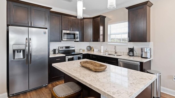 A modern kitchen with dark wood cabinets, stainless steel appliances, a marble countertop, and pendant lighting. - Modern 4BR Mid-City home with heated pool & balcony. Free parking, walk to streetcar & parades. (New Orleans)
