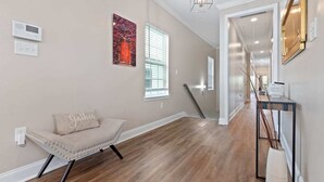 A hallway with a bench, a thermostat, a window with blinds, and a staircase. - Modern 4BR Mid-City home with heated pool & balcony. Free parking, walk to streetcar & parades. (New Orleans)