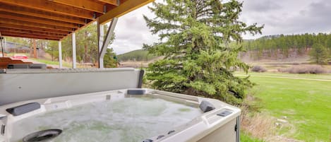 Ein Whirlpool unter einer Holzpergola mit Blick auf ein grasbewachsenes Feld und Bäume.