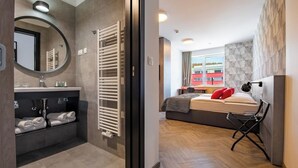 Een moderne hotelkamer met een groot bed, een stoel, een ingebouwde verwarming, een spiegel en uitzicht op een gebouw.