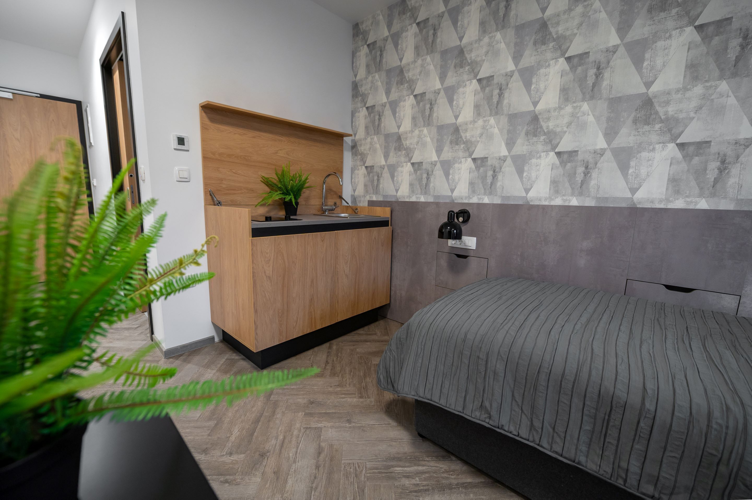 Un dormitorio con una cama, una mesita de noche de madera, un lavabo y un papel tapiz con estampado geométrico.