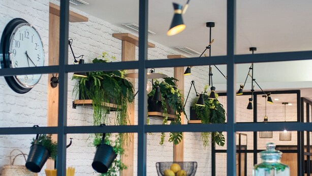 Een kamer met een witte bakstenen muur, een klok, hangende planten en hanglampen.