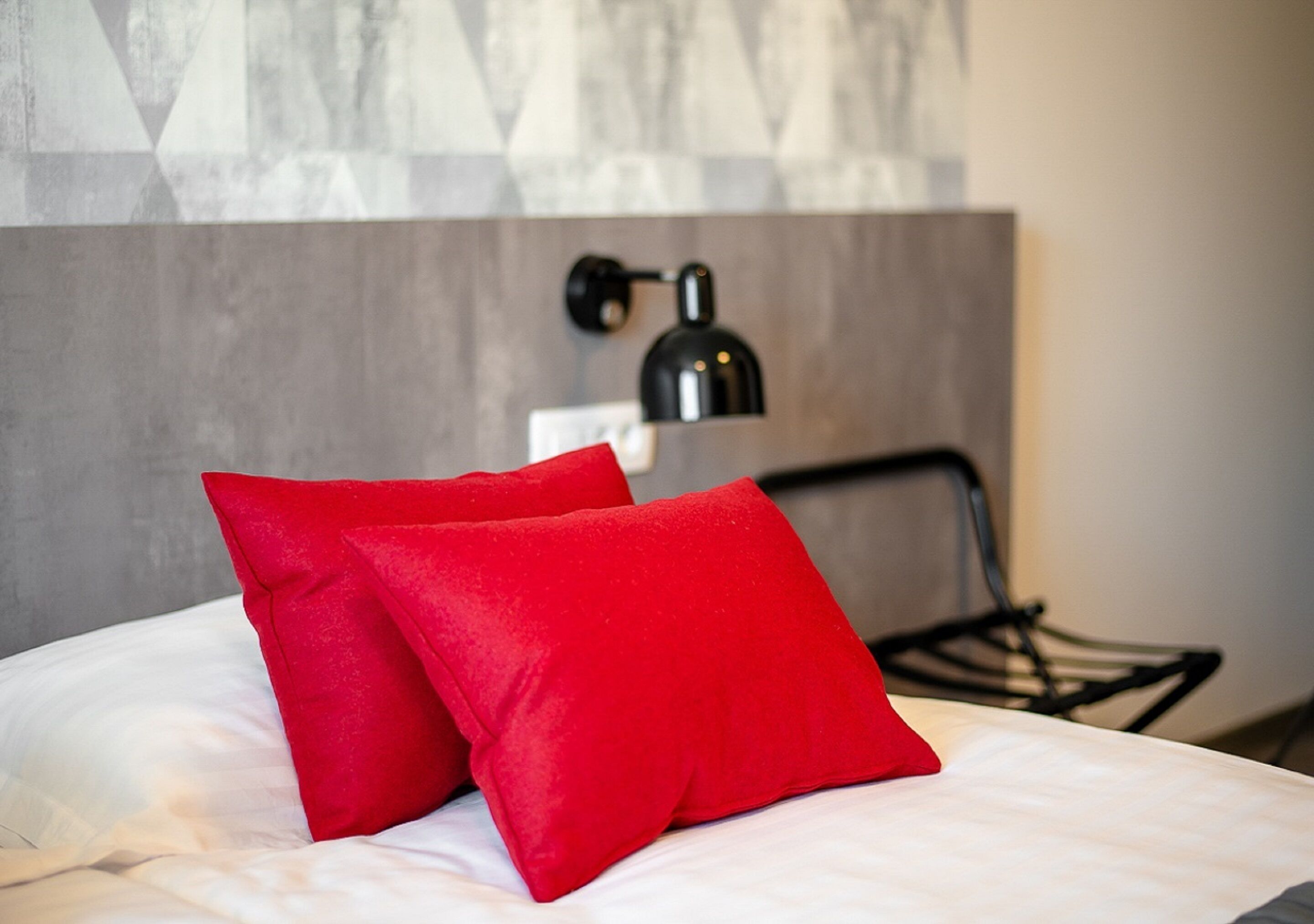 A bed with white bedding and two red pillows.