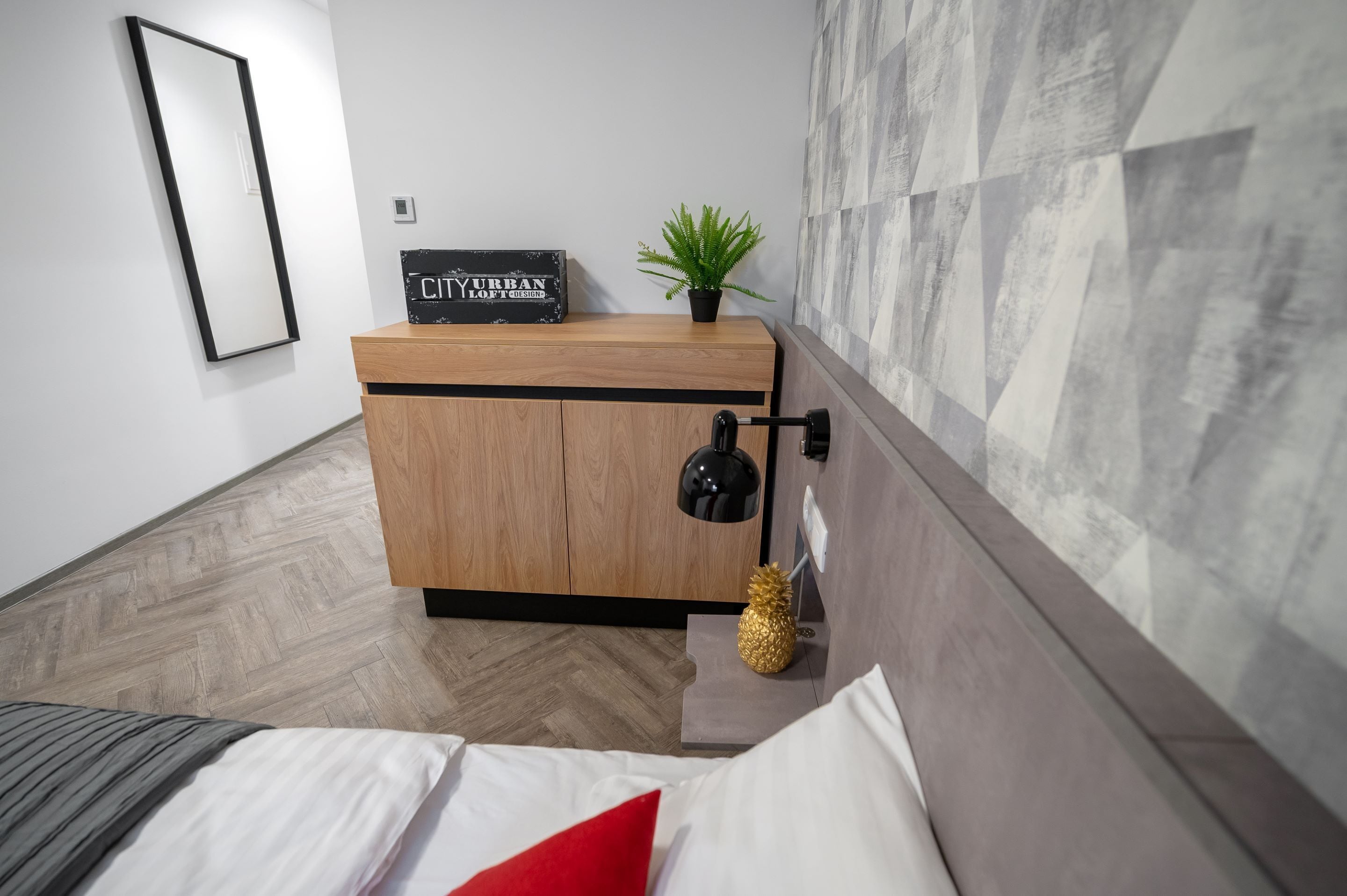 Ein modernes Schlafzimmer mit einem Bett, einem Nachttisch aus Holz, einer schwarzen Lampe und einem kleinen Topfpflanzen.
