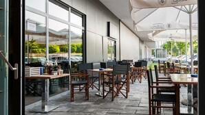 Een terras met tafels en stoelen, grote ramen en parasols.