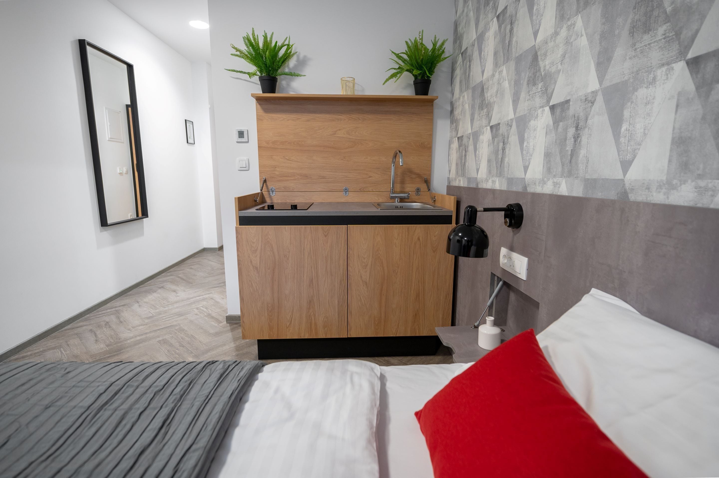 A modern hotel room with a wooden cabinet, a sink, and a bed with a red pillow.