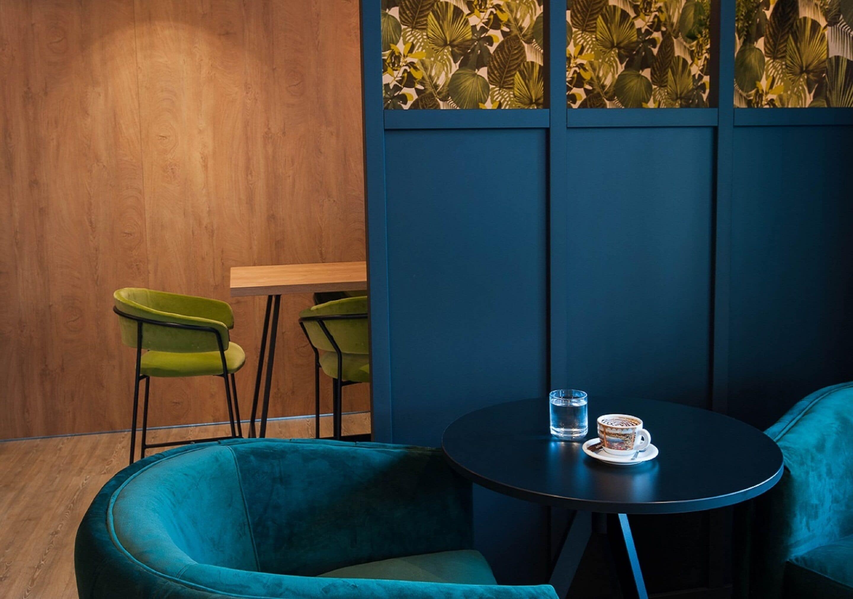 Un intérieur moderne avec un mur en bois, deux fauteuils verts, un canapé bleu et une table ronde sur laquelle se trouvent un verre et une tasse.