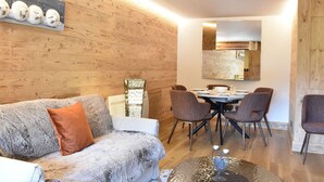 A cozy living room with a sofa, a coffee table, and a dining area with chairs and a table. - Meribel: Spacious 3BR Apartment, Sleeps 6, 150m from Ski Lift, Free Shuttle & Covered Parking (Méribel)