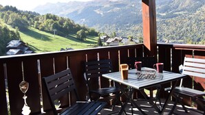 A wooden deck with a table and chairs overlooking a mountainous landscape. - Meribel: Spacious 3BR Apartment, Sleeps 6, 150m from Ski Lift, Free Shuttle & Covered Parking (Méribel)