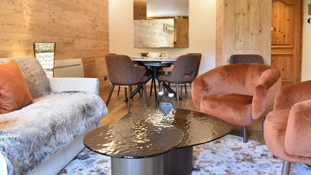 A cozy room with a wooden wall, a dining table with chairs, a sofa, and a coffee table. - Meribel: Spacious 3BR Apartment, Sleeps 6, 150m from Ski Lift, Free Shuttle & Covered Parking (Méribel)
