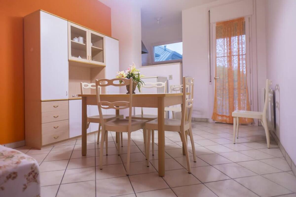 A dining area with a table and chairs, a cabinet with shelves, and a window with curtains.