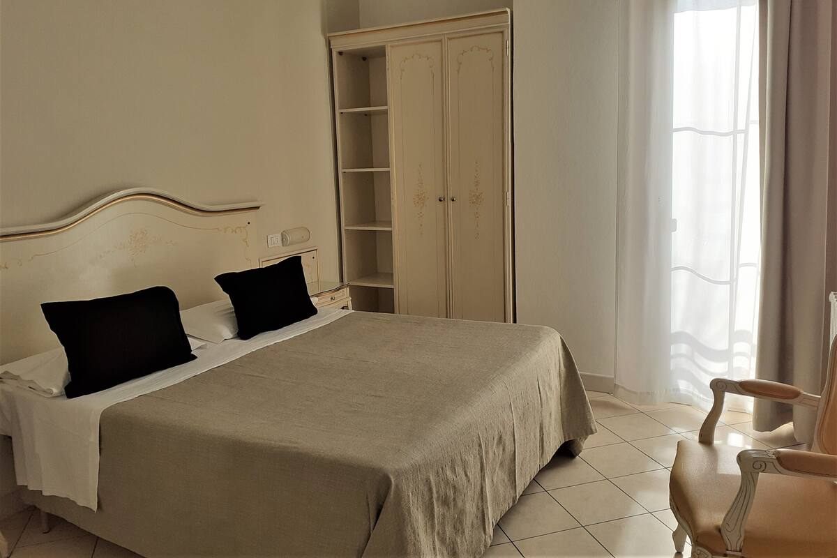 A bedroom with a bed, a wardrobe, a chair, and a window with curtains.