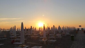 A beach with rows of sun loungers and umbrellas, a clear sky, and the sun setting in the background. - Ariston Vacanze Residence (Ravenna)