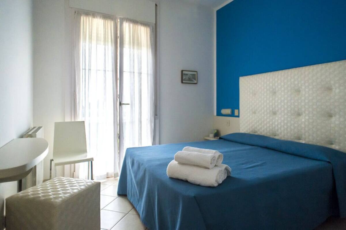 A hotel room with a bed, a chair, a small table, and a window with curtains.