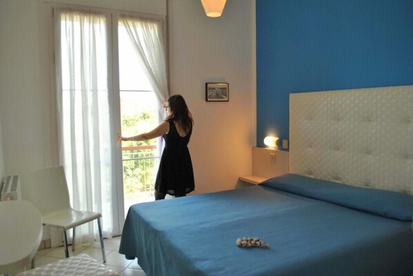 A bedroom with a bed, a chair, a table, and a window with curtains. - Ariston Vacanze Residence (Ravenna)