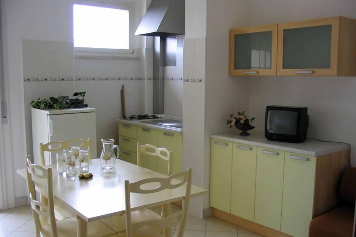 A compact kitchen with a dining area, featuring a refrigerator, stove, cabinets, and a television.