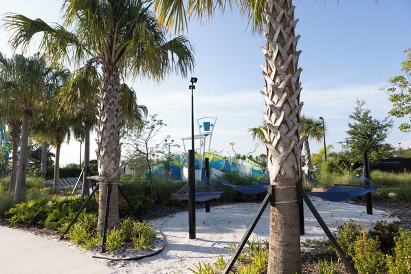 A landscaped area with palm trees, a hammock, and a playground with slides.