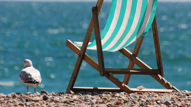A beach chair with a striped cover, a seagull, and a pebble beach with the ocean in the background.