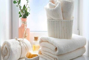 A stack of white towels, a woven basket, a glass jar with a cork, and a potted plant on a windowsill.